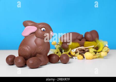 Schokoladen-Osterhasen und Eier auf weißem Tisch vor hellblauem Hintergrund Stockfoto