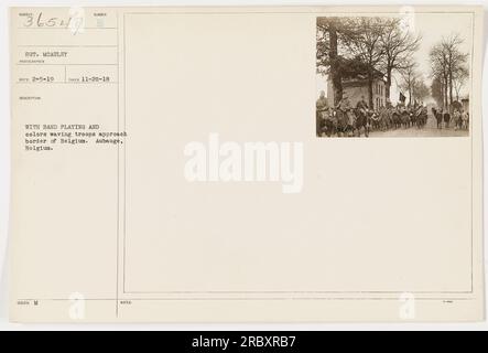 Truppen nähern sich der belgischen Grenze in Aubauge, während eine Band spielt und im Hintergrund Farben wehen. Das Foto wurde am 20. November 1918 von Sergeant McAuley, einem Militärfotografen, aufgenommen. Diese Informationen sind unter der Fotografienummer 111-SC-36547 in der Sammlung „Fotos der amerikanischen Militäraktivitäten während des Ersten Weltkriegs“ dokumentiert. Stockfoto