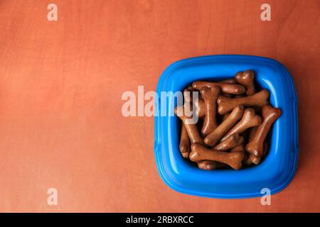 Blaue Schüssel mit knochenförmigen Hundekeksen auf einem Holztisch, Draufsicht. Platz für Text Stockfoto