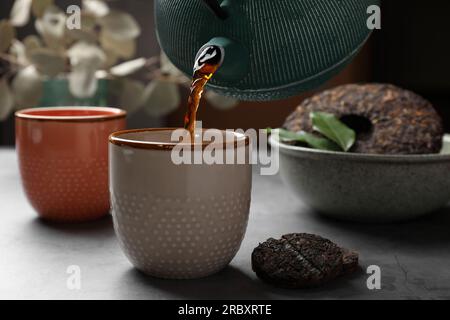 Frisch gebrühten pu-erh-Tee in eine Tasse auf einem grauen Tisch gießen, schließen Stockfoto