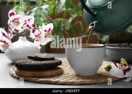 Frisch gebrühten pu-erh-Tee in eine Tasse auf einem grauen Tisch gießen, schließen Stockfoto