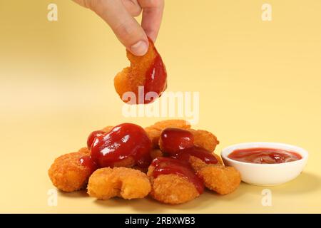 Eine Frau mit köstlichem Chicken Nugget mit Ketchup auf blassgelbem Hintergrund, Nahaufnahme Stockfoto