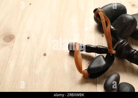 Schwarze Steinschleuder mit Steinen auf Holztisch, Nahaufnahme. Platz für Text Stockfoto