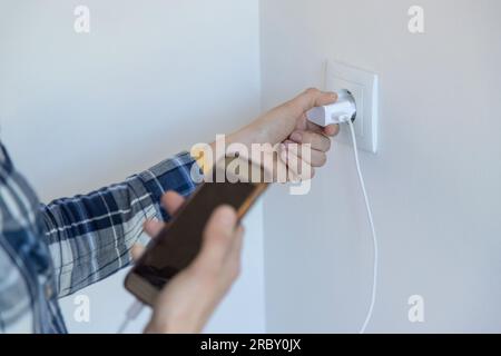 Nahaufnahme einer Person, die ein Smartphone und ein Ladegerät in der Hand hält, um es aufzuladen. Horizontaler Bild- und Kopierbereich. Stockfoto