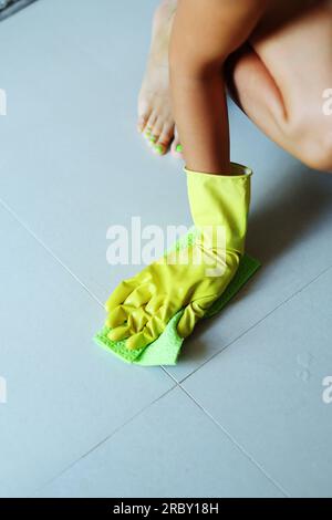 Die Hand einer Frau trägt gelbe Gummihandschuhe mit einer Bürste, um den Fliesenboden zu schrubben, Hausfrau, Hausarbeit Stockfoto