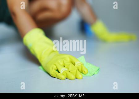 Die Hand einer Frau trägt gelbe Gummihandschuhe mit einer Bürste, um den Fliesenboden zu schrubben, Hausfrau, Hausarbeit Stockfoto