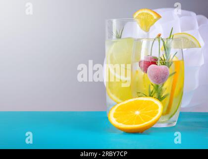 Getränke mit Zitrusscheiben und Kirschen in Glasgläsern auf grauem Hintergrund mit horizontalem Kopierbereich Stockfoto
