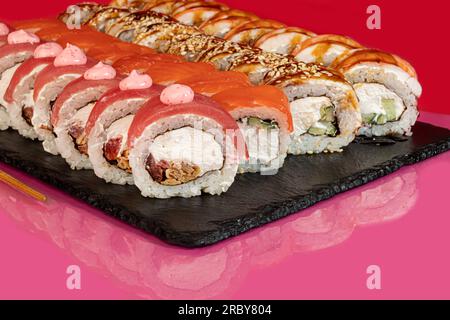 Sushi-Sets, Brötchen mit Kaviar, Garnelen, Thunfisch und Avocado und Philadelphia-Käse auf einem weißen Teller. Auf einem farbigen Hintergrund. Speicherplatz kopieren Stockfoto