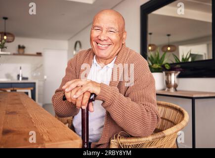 Porträt, Gehstock und ein älterer Mann mit einer Behinderung, der während seines Ruhestands im Wohnzimmer seines Hauses sitzt. Lächeln, Stock und entspannen Sie sich mit einem Stockfoto