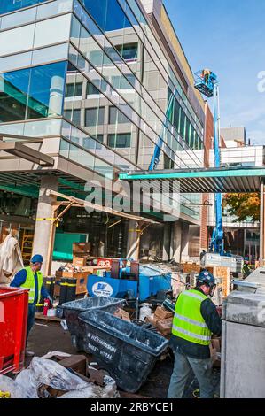 Drei Arbeiter befinden sich auf Bodenhöhe, zwei Arbeiter in einem Personenlift oder einem Kirschsammler, während sie am Bau einer Gesundheitseinrichtung arbeiten. Stockfoto