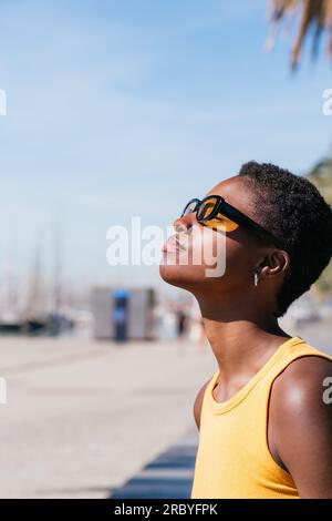 Vertikales Porträt von einer Seite einer afrikanerin mit sehr kurzen Haaren. Sie sieht weg und genießt die Sonne Stockfoto