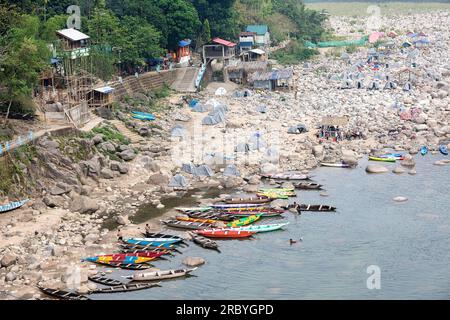 Traditionelle farbenfrohe Holzboote auf dem Dawki-Fluss, die an einem Flussufer in der Nähe der Dawki-Stadt, Meghalaya, Indien, geparkt sind Stockfoto