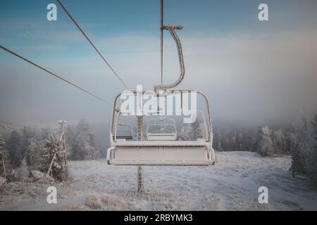 Sonnenaufgang bricht durch den dicken weißen Nebel auf dem Gipfel des Vuokatti Hill, einem Skigebiet in Vuokatti, Finnland. Blick auf den gefrorenen Sessellift. Die Scand Stockfoto