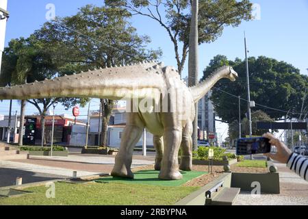 Stadt: Marilia, São Paulo, Brasilien - 2023. Juli 2023 : Nachbildung eines Dinosauriers auf einem Stadtplatz im Inneren von São Paulo mit Touristen, die Fotos machen Stockfoto