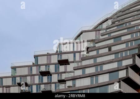 Blick aus der Perspektive eines flachen Engels auf einen minimalen modernen Wolkenkratzer mit horizontalem Glasgeländer vor dem Balkon des gesamten Gebäudes. Stockfoto