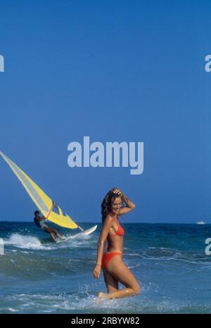 Glückliche, hübsche junge Frau, die auf Wellen spielt, Meerwasser und blauer Himmel auf dem Hintergrund sehr gesundes, attraktives Gesicht mit Windsurfer Sommerferien Stockfoto