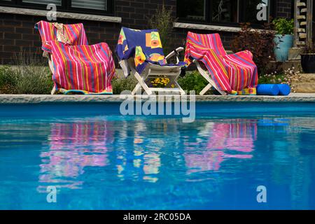 Pinkfarbene Strandtücher spiegeln sich im blauen Wasser des Swimmingpools im Garten mit Garten wider Stockfoto