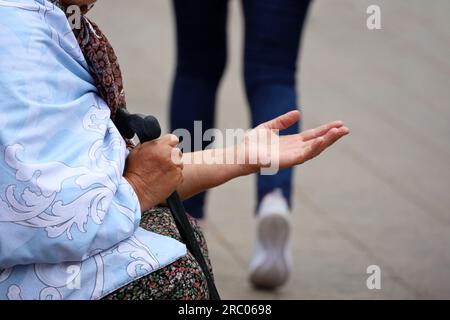 Die alte Bettler bittet um Almosen, die auf einer Straße mit ausgestreckter Hand sitzen. Armut, Obdachlosigkeit und Bettelei Stockfoto