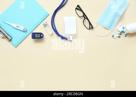 Badge, Pulsoxymeter, Schutzbrille, Pillen, Klemmbrett und Maske auf beigefarbenem Hintergrund Stockfoto