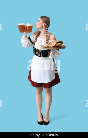 Wunderschöne Oktoberfest-Kellnerin mit Bier und Snacks auf blauem Hintergrund Stockfoto