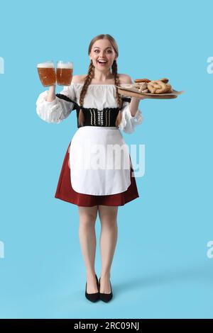 Wunderschöne Oktoberfest-Kellnerin mit Bier und Snacks auf blauem Hintergrund Stockfoto