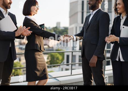 Eine Vielzahl von Geschäftsleuten in formeller Kleidung, die erfolgreich Geschäfte abschließen und sich über die Zusammenarbeit freuen. Kaukasische und afroamerikanische Kollegen schütteln sich nach Verhandlungen die Hand. Partnerschaftskonzept. Stockfoto