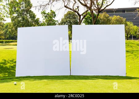 Zwei leere quadratische weiße Reklametafeln stehen in der Sonne auf dem grünen Gras eines thailändischen Golfplatzes. Stockfoto