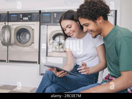Glückliches Lateinamerikanisches Paar, Das Beim Wäschen Im Haus Ein Digitales Tablet Benutzt Stockfoto