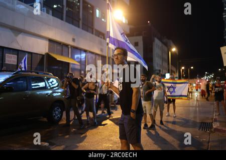 Tel Aviv, Israel. 11. Juli 2023. Israelische Demonstranten halten während eines Protests nach der Abstimmung in der Knesset gestern Abend die Flagge. Das israelische parlament hat trotz massiver Proteste gegen die Pläne die erste Lesung eines Gesetzentwurfs über kontroverse Justizreformen gebilligt. Kredit: Ilia Yefimovich/dpa/Alamy Live News Stockfoto