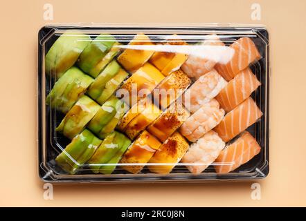 Ein Set aus hellen, mehrfarbigen Sushi-Brötchen mit Garnelen, Lachs, Aal, Avocado, Käse in Kunststoffverpackung, auf hellem Hintergrund, Draufsicht. Stockfoto