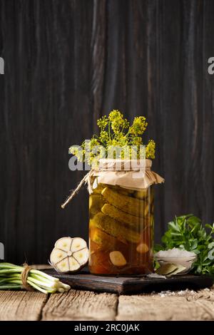 Eingelegte Gurken in einem Glas, frische Cornflakes, Knoblauch auf Holzhintergrund. Paprika, Zwiebeln und frische Cornichons zur Konservierung. Gurkensalat. Stockfoto