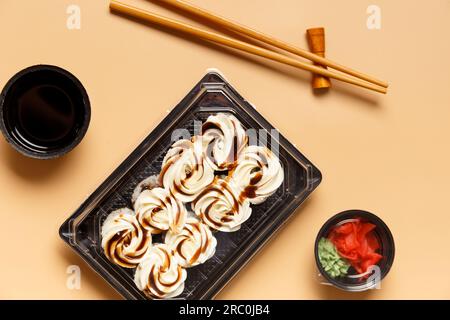 Sushi-Brötchen mit Lachs, garniert mit Frischkäse und Sauce in einer Plastikpackung, Essstäbchen, Ingwer, Sauce auf hellem Hintergrund. Stockfoto