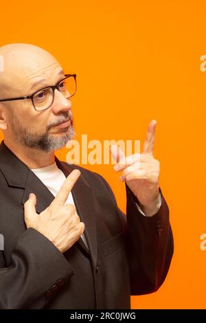 Eleganter Mann in einer Anzugjacke, bärtig, kahl und mit Brille. Isoliert auf orangefarbenem Hintergrund Stockfoto