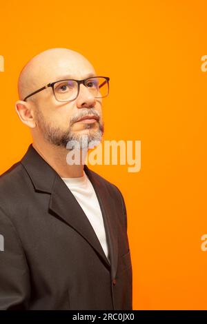 Eleganter Mann in einer Anzugjacke, bärtig, kahl und mit Brille. Isoliert auf orangefarbenem Hintergrund Stockfoto