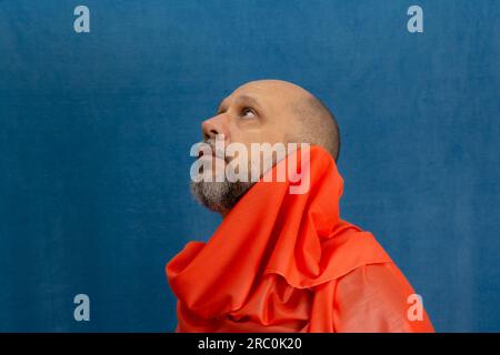 Ein kahlköpfiger, bärtiger Mann, der ein orangefarbenes Tuch um den Hals trägt. Isoliert auf blauem Hintergrund. Stockfoto