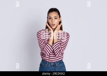 Shocked emotional young woman holding hands next to face Stockfoto