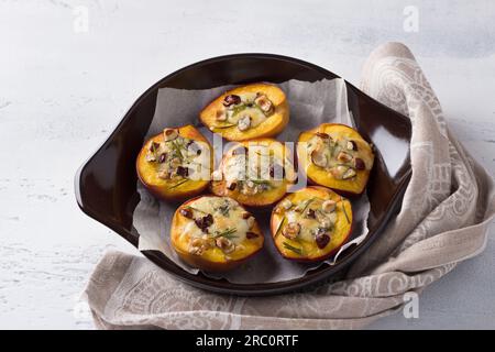 Pfirsiche gefüllt mit blauem Käse mit Nüssen und Rosmarin in einer Backform auf hellgrauem Hintergrund, Draufsicht. Köstliches Gourmet-Dessert. Stockfoto
