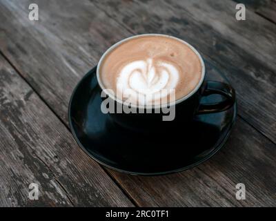 Eine Kaffeekunst in Vintage-Farben in einem schwarzen Becher auf einem alten Holztisch Stockfoto