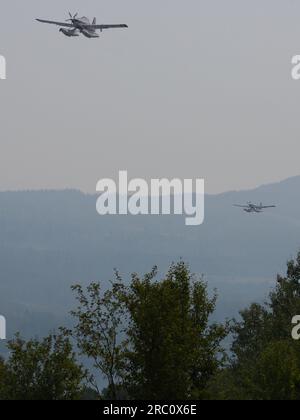 Zwei Wasserbombenflugzeuge bekämpfen Waldbrände in der Nähe von Smithers während des Fluges, nachdem sie Wasser vom nahe gelegenen Tyhee Lake aufgesammelt haben. - Smithers v. Chr. - 09 2023. Juli Stockfoto