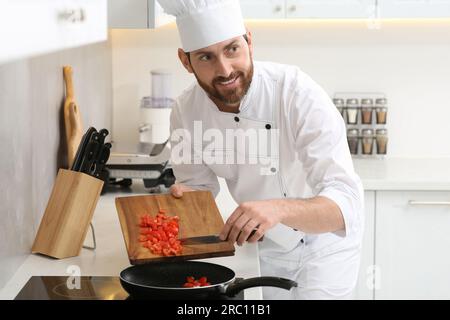 Glücklicher Koch, der im Haus geschnittene Tomaten in die Bratpfanne gab Stockfoto