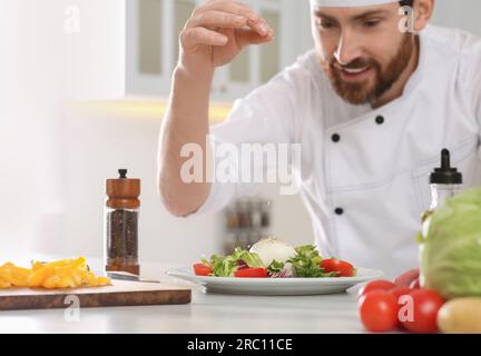 Professioneller Koch salzt köstlichen Salat am Marmortisch, Fokus auf Essen Stockfoto