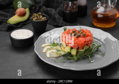 Köstliches Lachs-Tartare mit Avocado und Zitrone auf einem dunklen Tisch Stockfoto