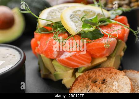 Köstliche Lachs-Tartare mit Avocado, Sauce und Croutons auf dunklem Brett, Nahaufnahme Stockfoto