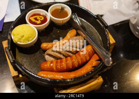 Barbecue-Würstchen und Sauce auf dem Teller auf schwarzem Steinhintergrund mit Seitenansicht des Kopierbereichs Stockfoto