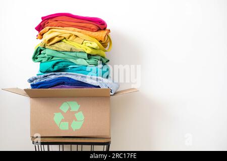 Ein Stapel Kleidung in verschiedenen Farben in einer Schachtel mit einem Recycling-Schild. Stockfoto