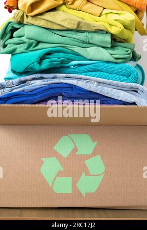 Ein Stapel Kleidung in verschiedenen Farben in einer Schachtel mit einem Recycling-Schild. Stockfoto