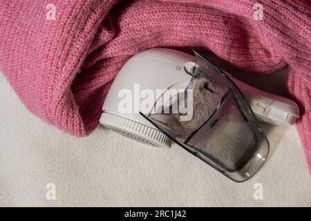 Anti-Pilling-Rasierer. Gerät zum Rasieren von Kleidung. Anti-Plush-Rasierer. Elektrischer tragbarer Pullover, Pille, Entfärbung, Fusselentferner aus pinkfarbenem Acryl- oder Wollpullover. Elektrorasierer nach der Reinigung und aufgefangenen Fusseln. Ein Pullover aus der Nahaufnahme. Alte gebrauchte Kleidung mit Pillen. Stockfoto
