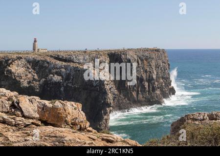 Surfen Sie auf felsigen Klippen im Atlantik und auf dem Leuchtturm Farol de Sagres an der Stelle der Festung Fortaleza de Sagres, Ponta da Sagres, Faro Stockfoto