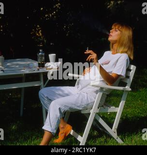 Schwangere Frau am Gartentisch mit Zigaretten und Alkohol, Rauchen während der Schwangerschaft Stockfoto