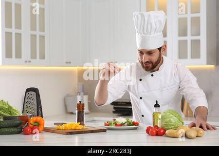 Professioneller Koch salzt köstlichen Salat am Marmortisch in der Küche. Platz für Text Stockfoto